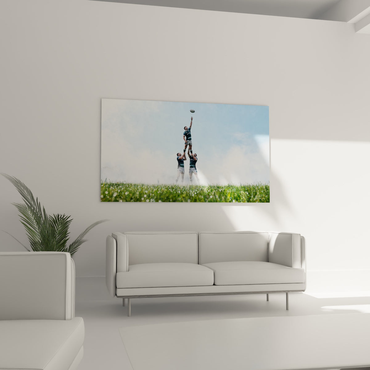 Scène de touche au rugby, vert du terrain et bleu du ciel, accrochée au-dessus d'un canapé dans un salon lumineux