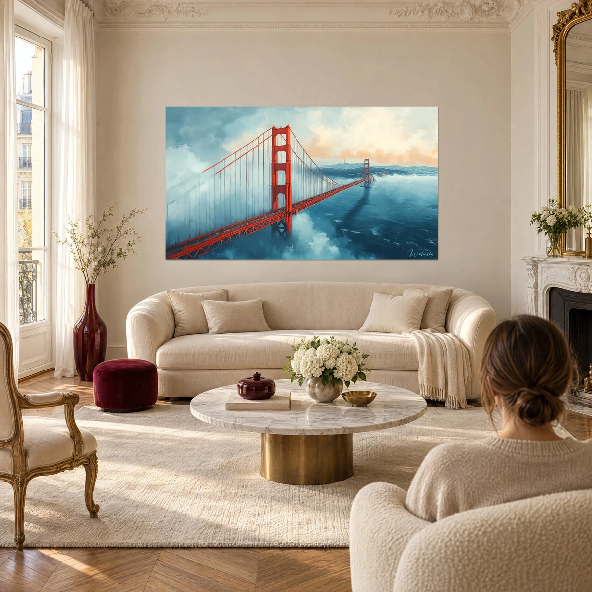 Cuadro Golden Gate en rojo bermellón emergiendo de una bruma azul petróleo, una mujer de espaldas, encima de un sofá en un salón luminoso