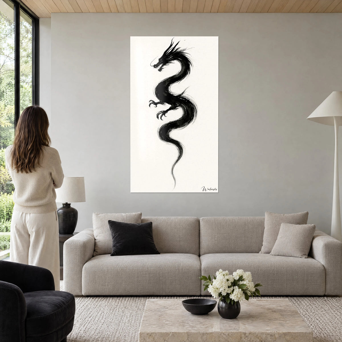 Obraz chiński smok w czarnym tuszu z rozpostartymi szponami na kremowym tle, kobieta tyłem, nad kanapą w jasnym salonie