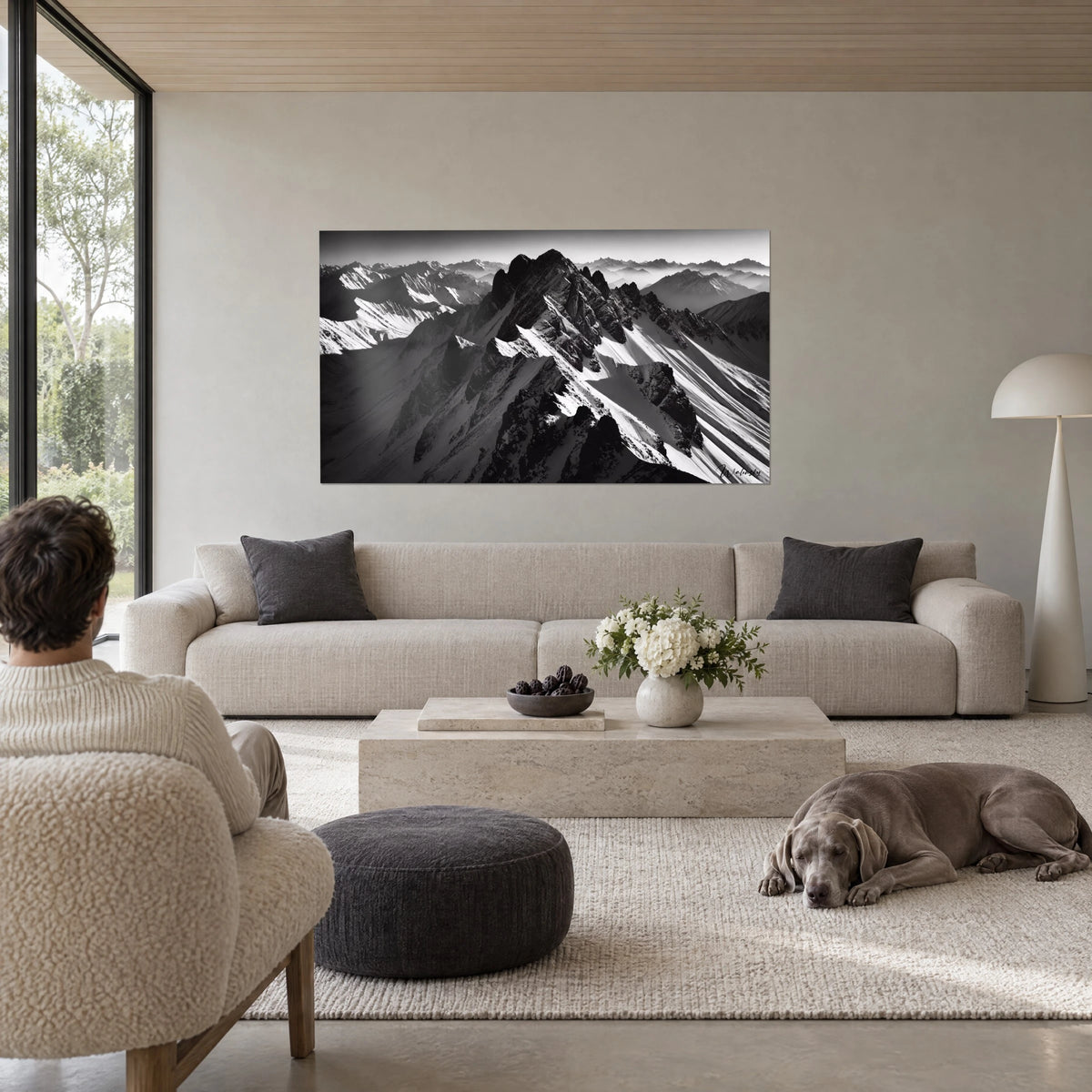 Wall art snowy alpine ridge in black and white, grey arêtes on white snow, man seen from behind, above a sofa in a bright living room