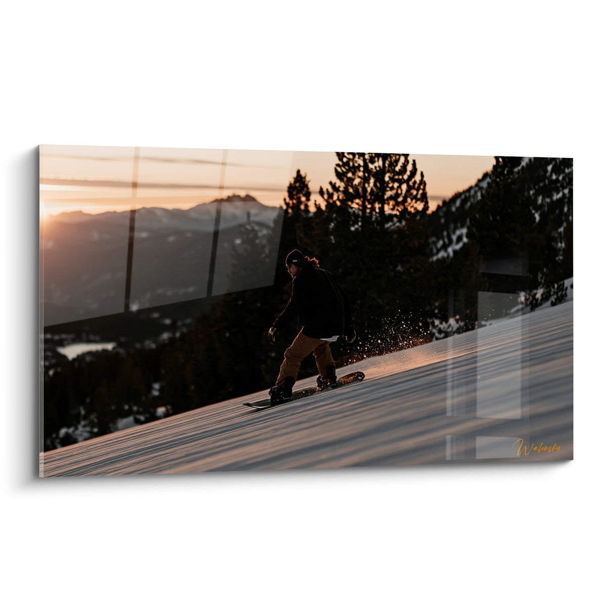 Snowboardeur en silhouette noire dévalant une pente enneigée sous un ciel orange et doré au crépuscule