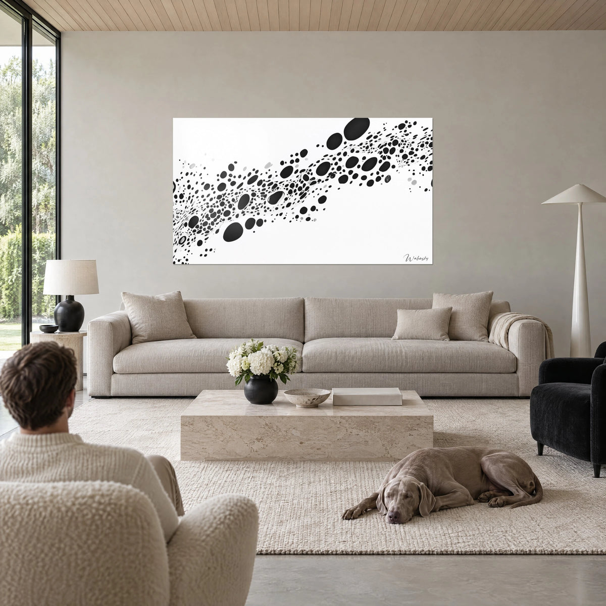Tableau traînée de taches d'encre noires sur fond blanc, ovales et gouttelettes, homme et chien, au-dessus d'un canapé dans un salon lumineux