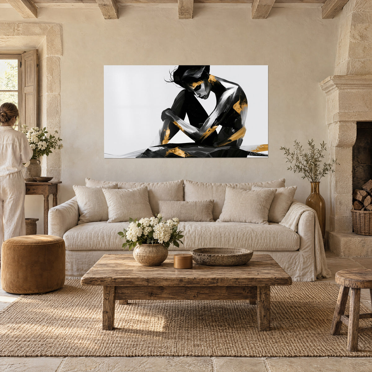 Wall art crouched silhouette with black and gold brushstrokes on a white background, with a woman seen from behind, above a sofa in a bright living room