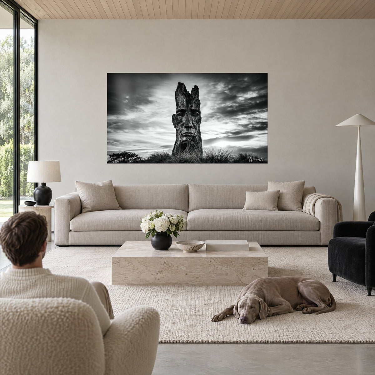 Tableau visage sculpté dans un tronc, noir et blanc, ciel d'orage contrasté, homme de dos, au-dessus d'un canapé dans un salon lumineux