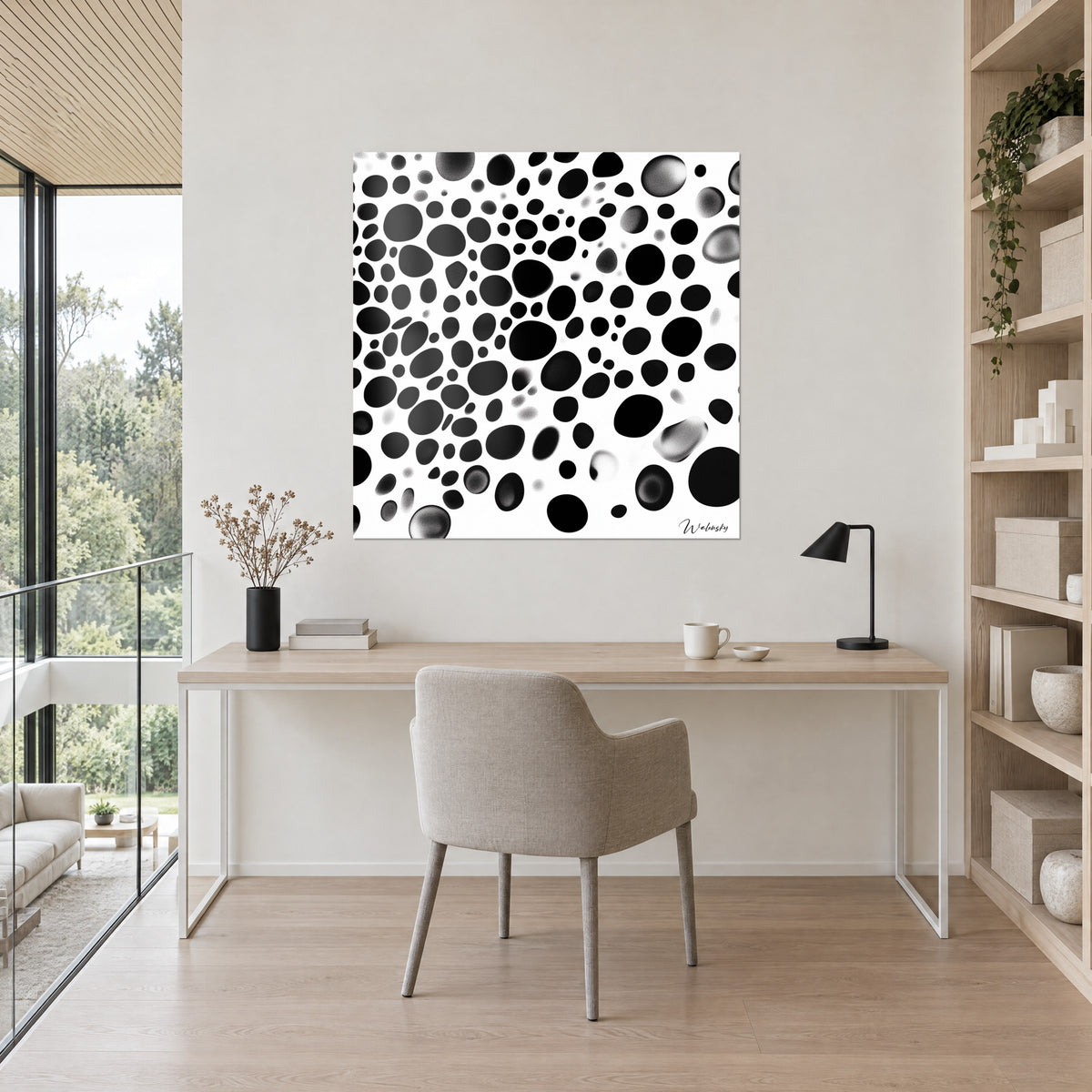 Wall art with a constellation of black and graded grey pebbles on white, ivory wall above a light wood desk and a beige chair
