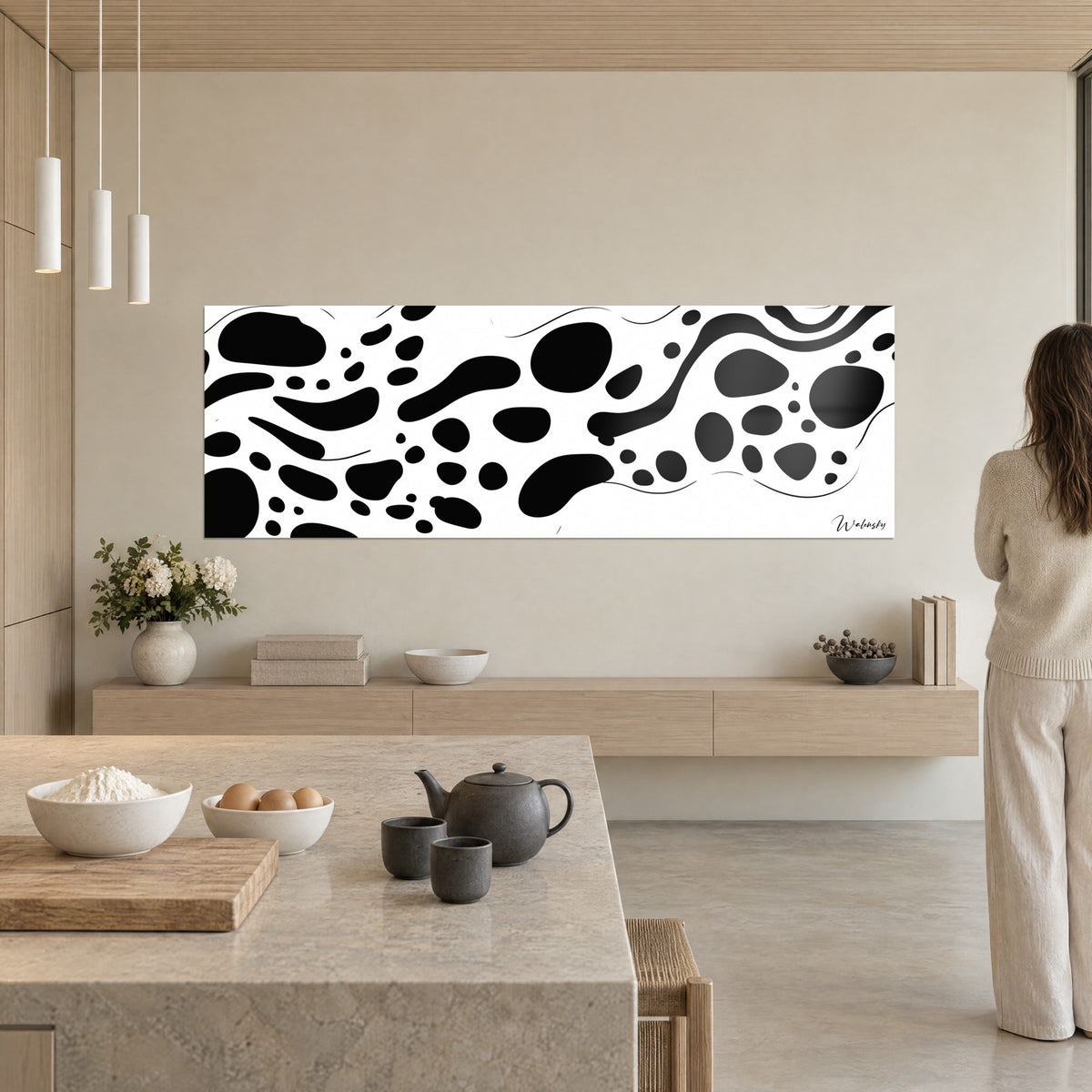 Quadro arte maculata primitiva, ciottoli d'inchiostro neri su bianco puro, sulla parete di una cucina beige e legno, donna di spalle
