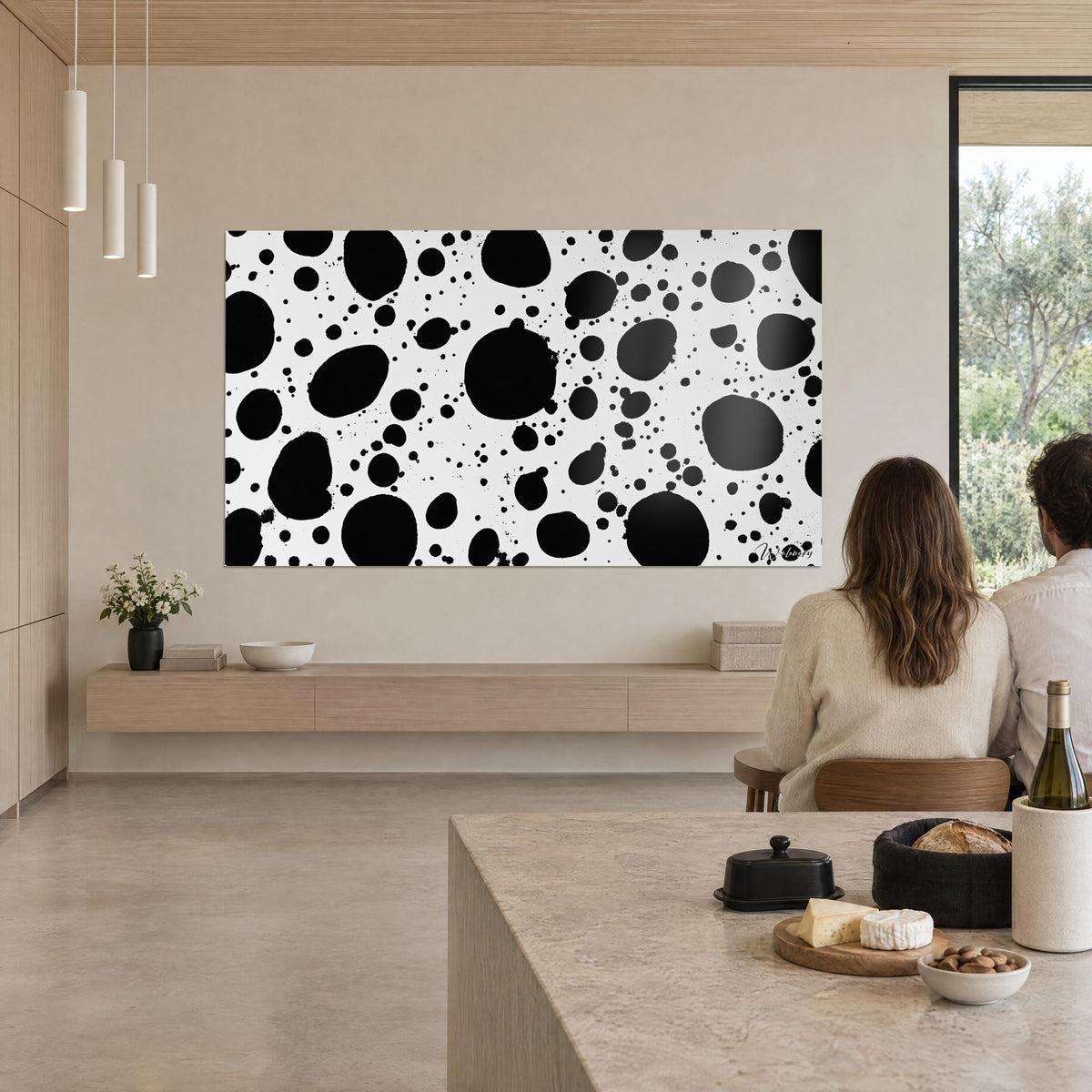 Wall art with black ink splatters on white, large bubbles and fine sprays, facing a beige stone table and floor-to-ceiling windows