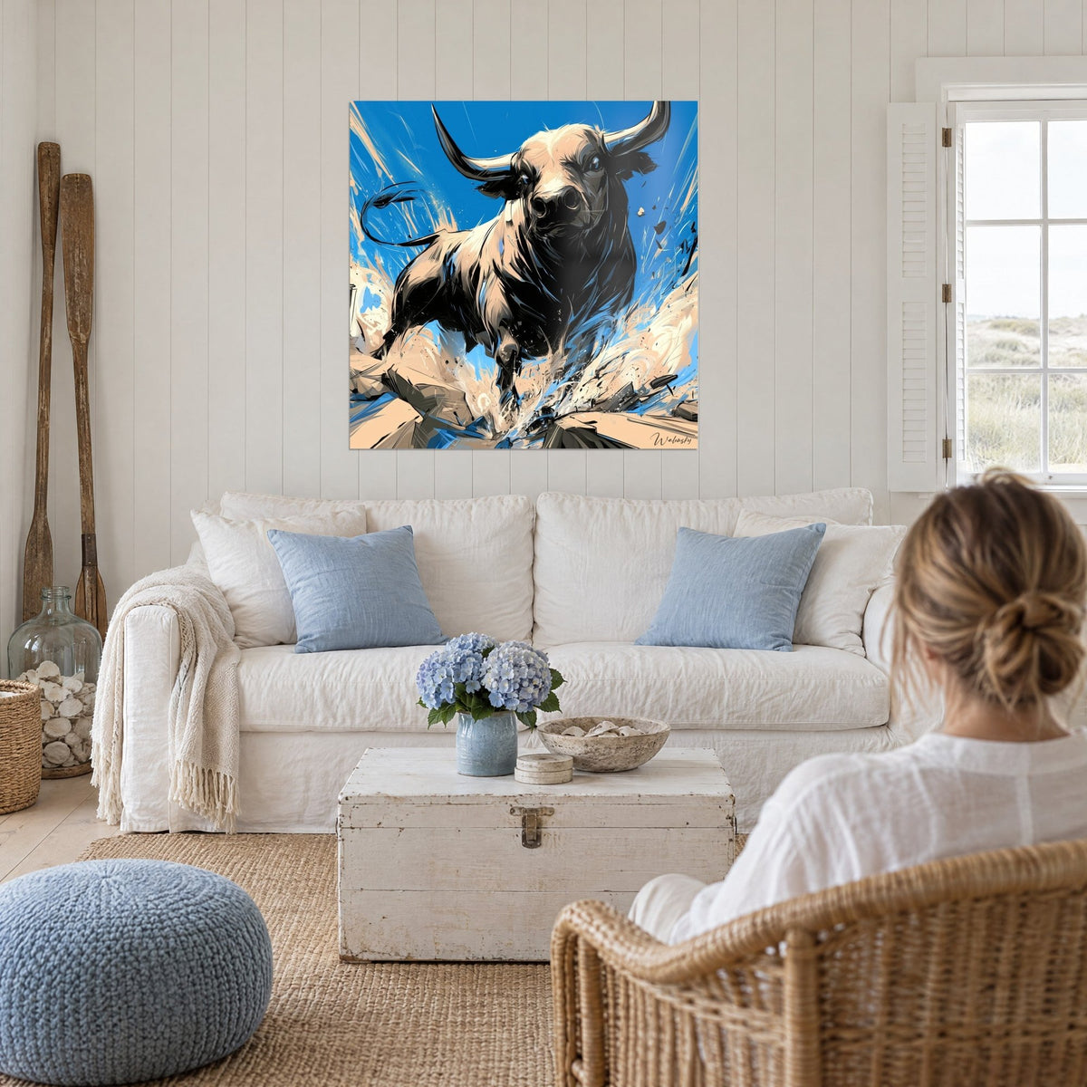 Schilderij zwarte stier met opgeheven hoorns op felblauwe achtergrond, beige splinters, jonge vrouw van achteren, boven een bank in een lichte woonkamer
