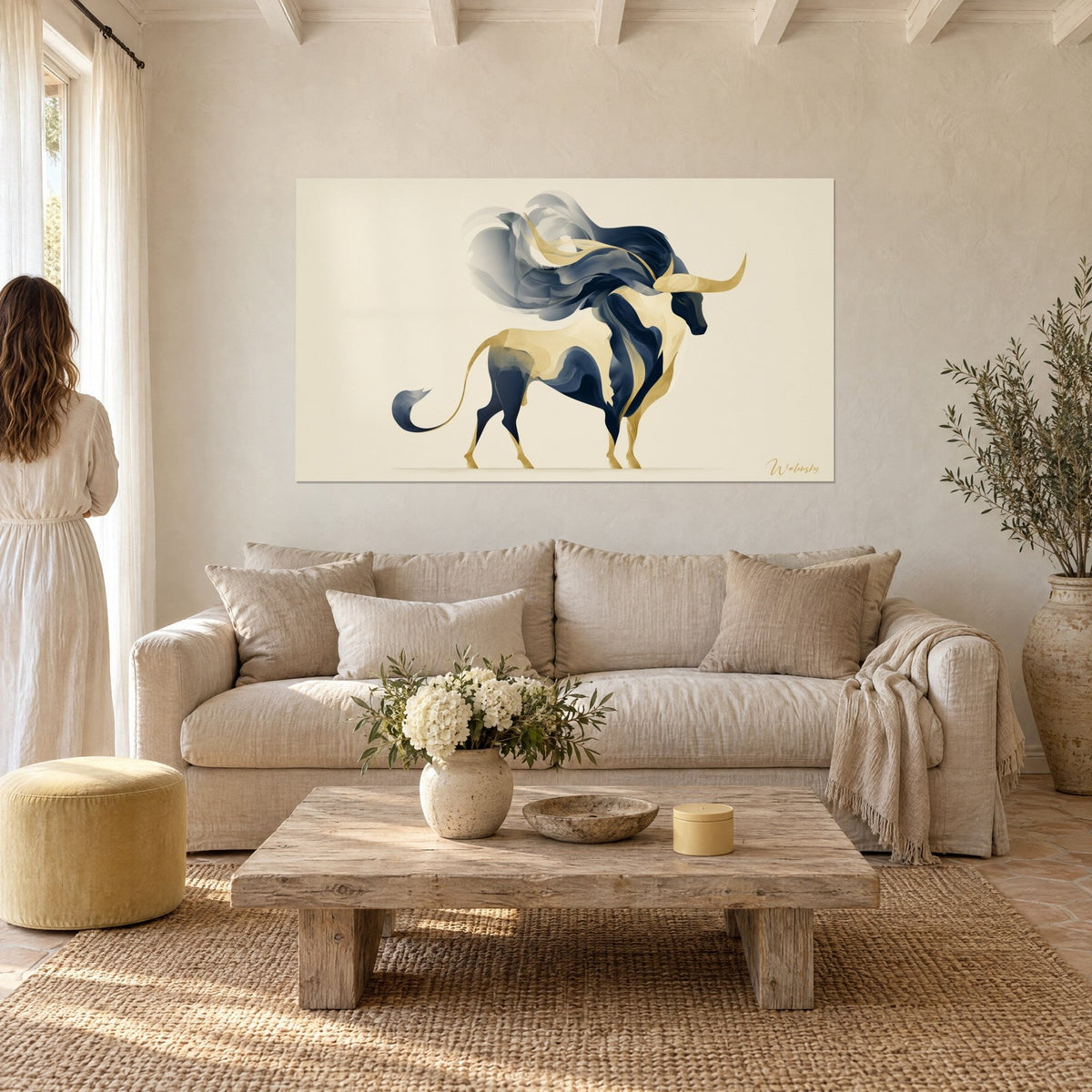 Quadro di un toro stilizzato blu notte e oro, criniera grigio fumo, una donna di schiena sopra un divano in un soggiorno luminoso