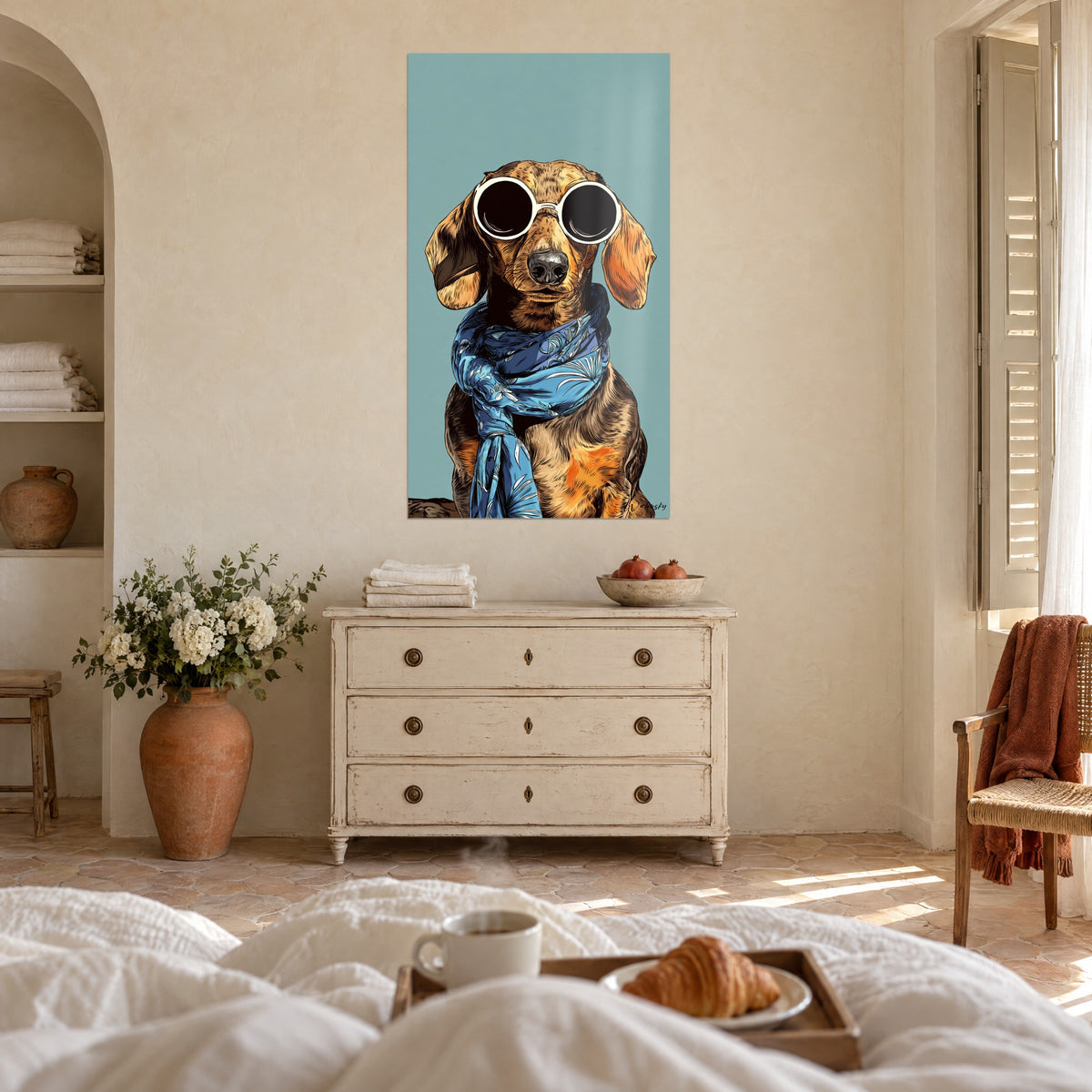 Cuadro teckel con lentes negras ribeteadas en blanco, pañuelo azul floreado, fondo turquesa, encima de una cama en un dormitorio luminoso