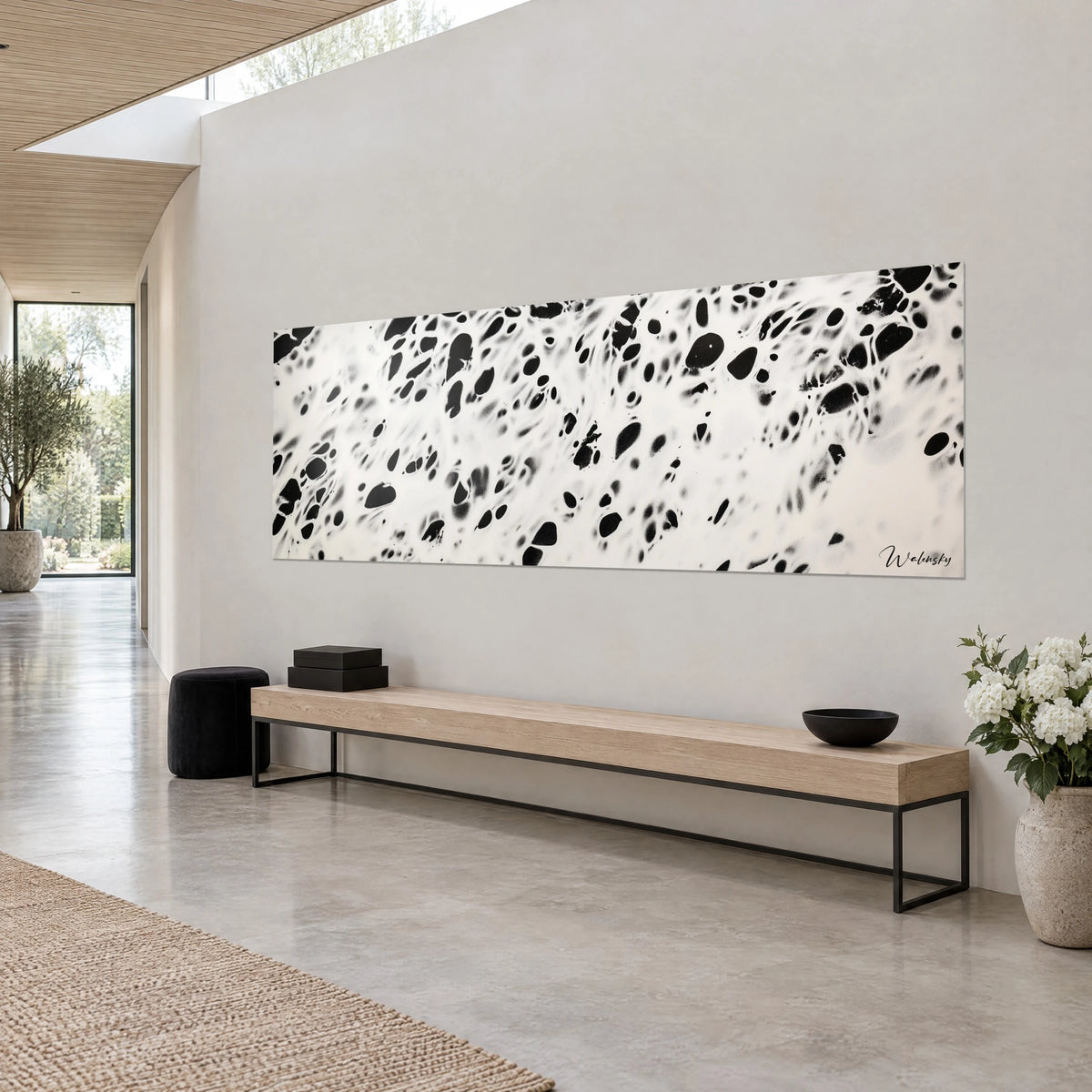 Tableau panoramique tacheté noir et blanc, éclaboussures d'encre sur fond ivoire, mur gris, banc en bois et ottoman noir