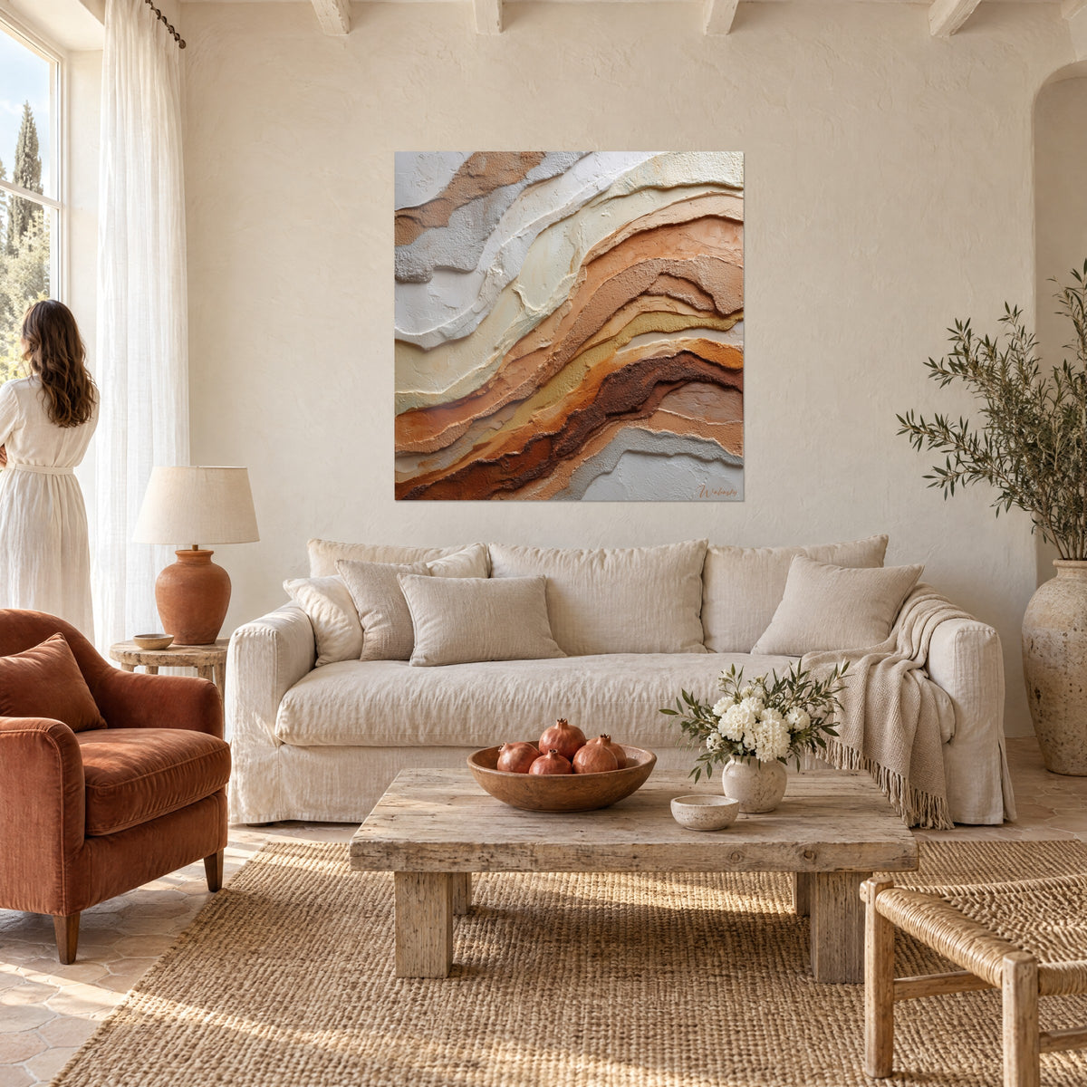 Quadro con strati minerali in rilievo, fasce color crema e terracotta, donna di spalle in primo piano, sopra un divano in un soggiorno luminoso