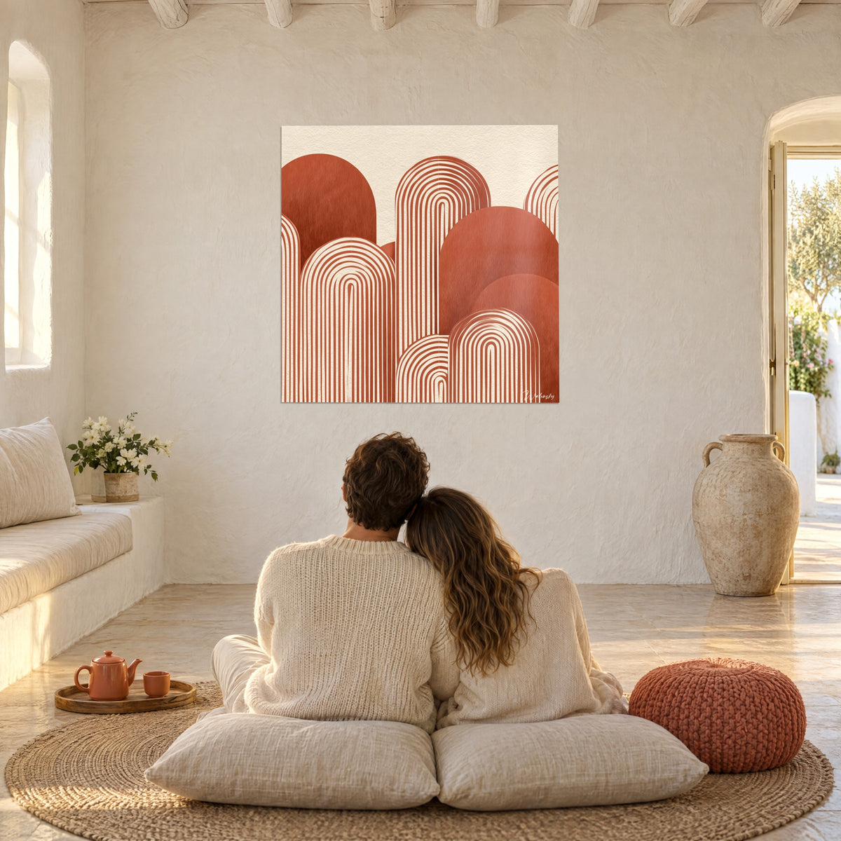 Tableau collines arrondies en arceaux brique et crème, sur mur blanc chaulé, devant un couple de dos sur des coussins au sol