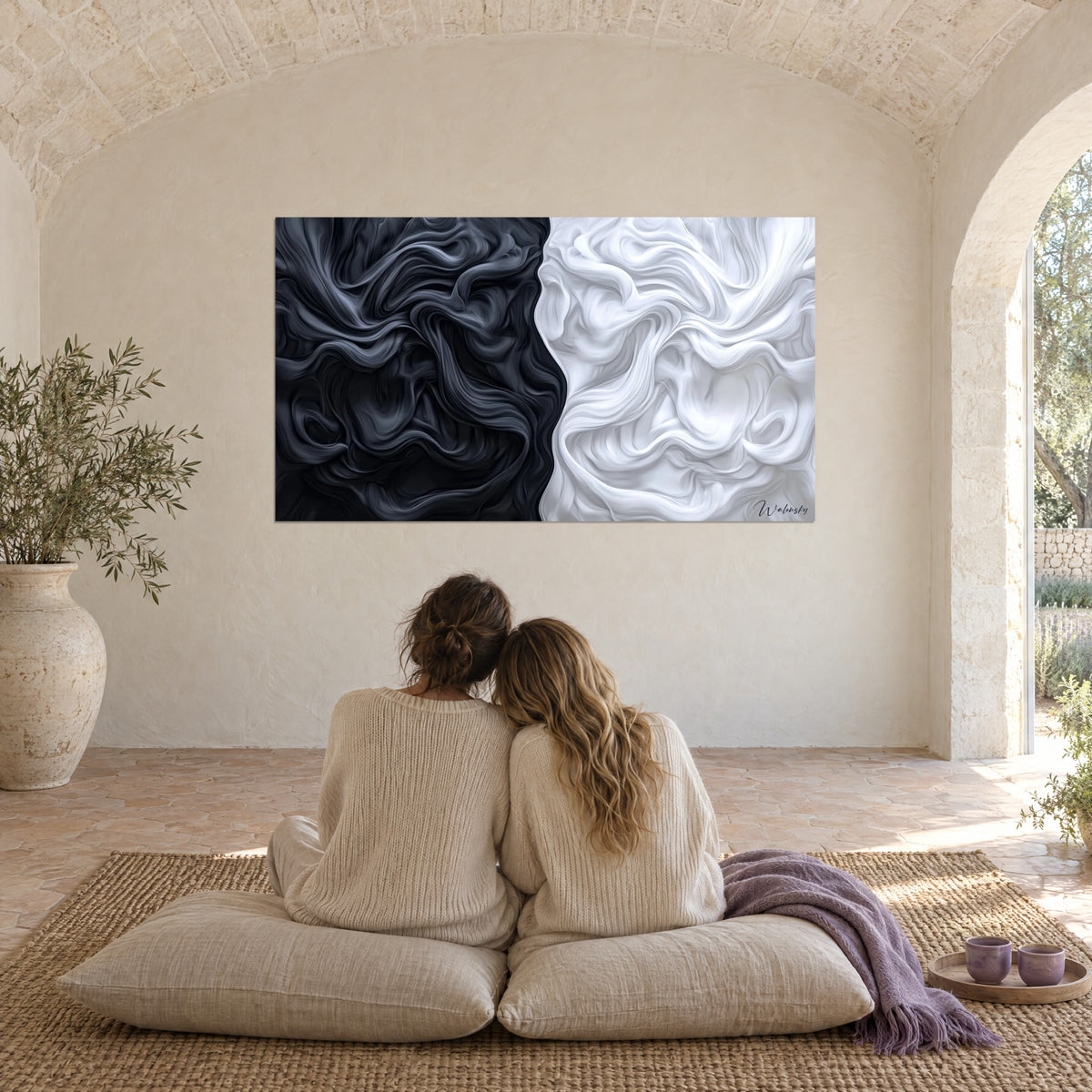 Wall art of contrasting bluish-black and milky-white waves, gazed at by two embracing women seated on cushions