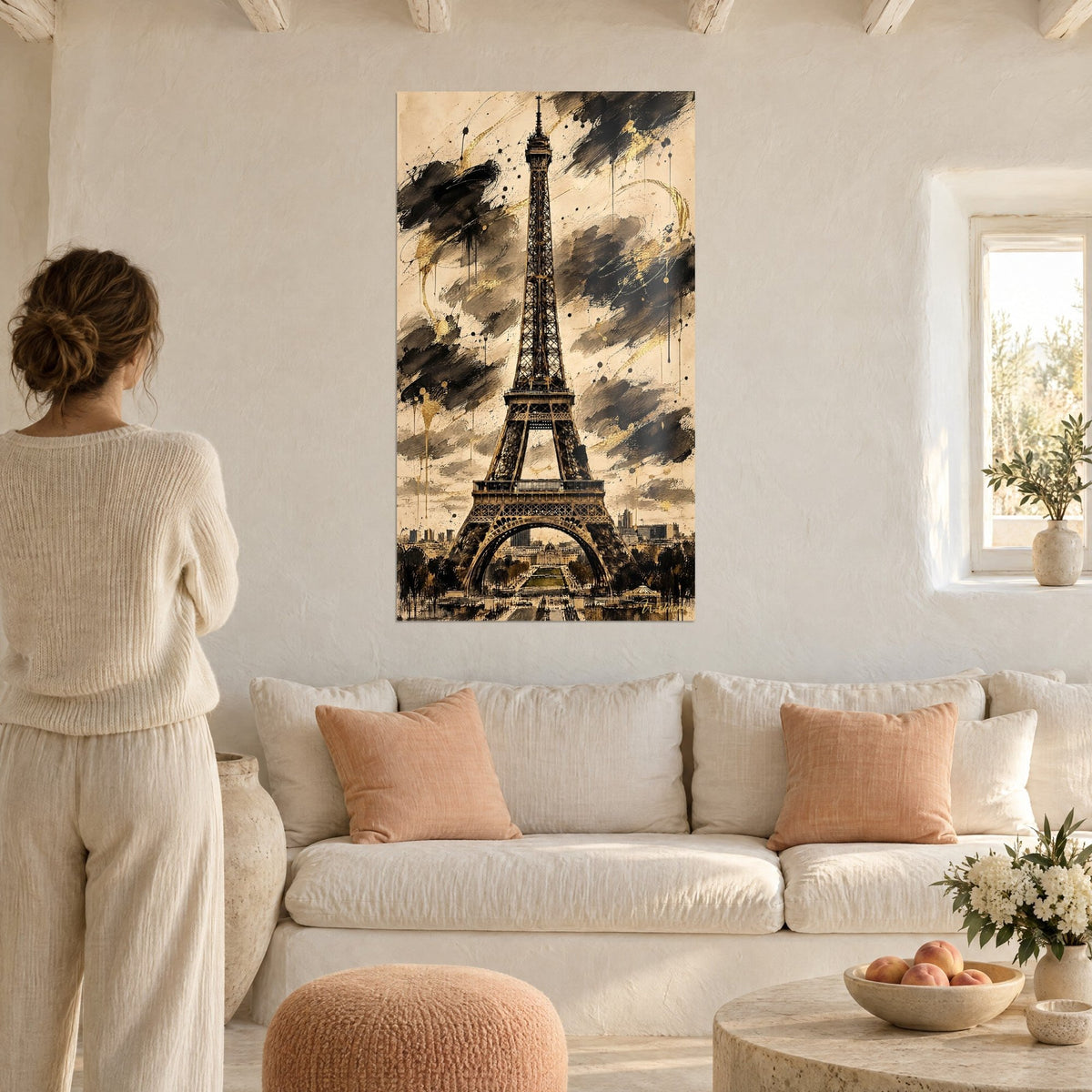 Schilderij Eiffeltoren in sepia met zwarte inktwolken en gouden druipsporen, vrouw van achteren, boven een bank in een lichte woonkamer