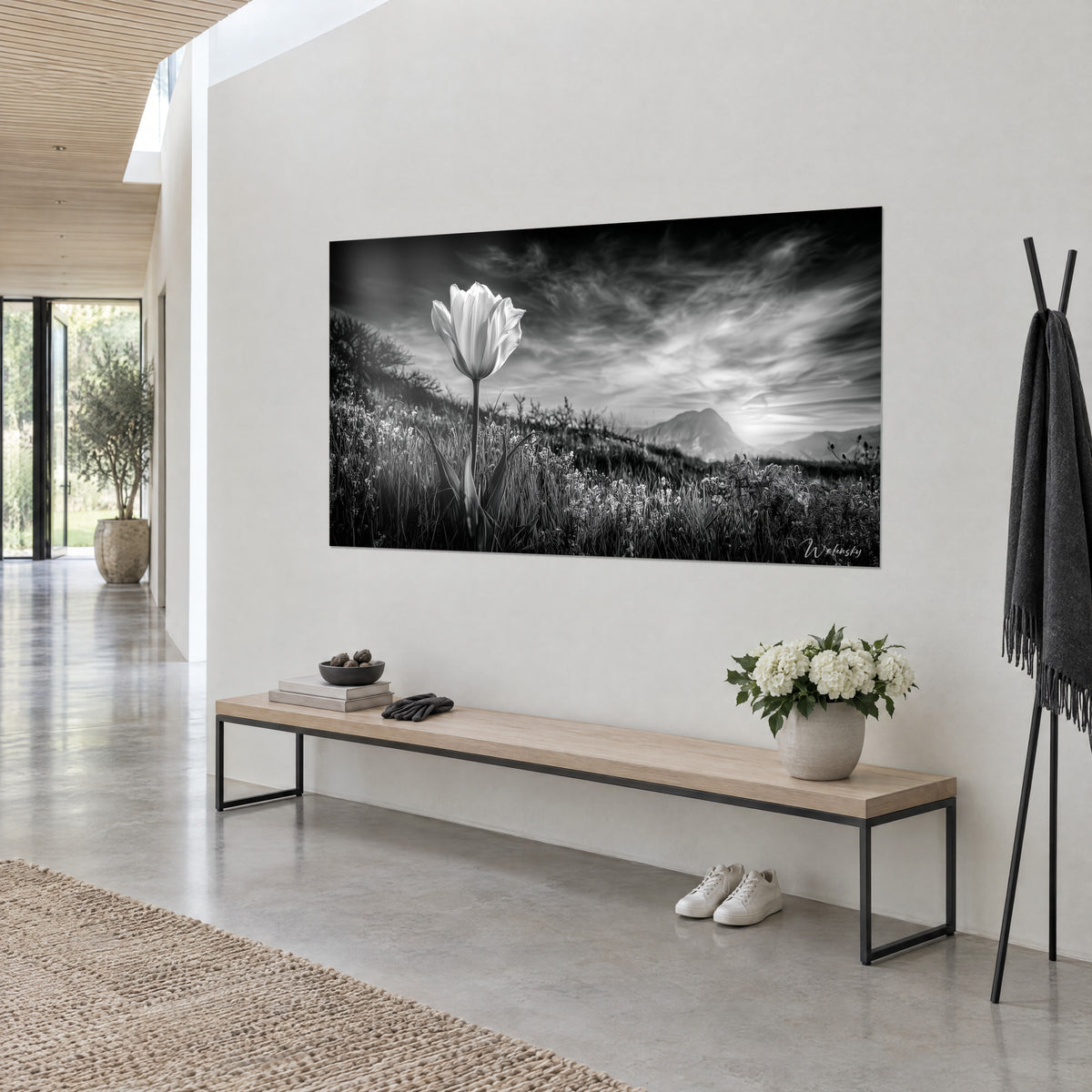 Tableau fleur immaculée sur longue tige, nuages striés noir et gris perle, montagne au loin, vue de trois-quarts sur un mur blanc au-dessus d'un banc en bois