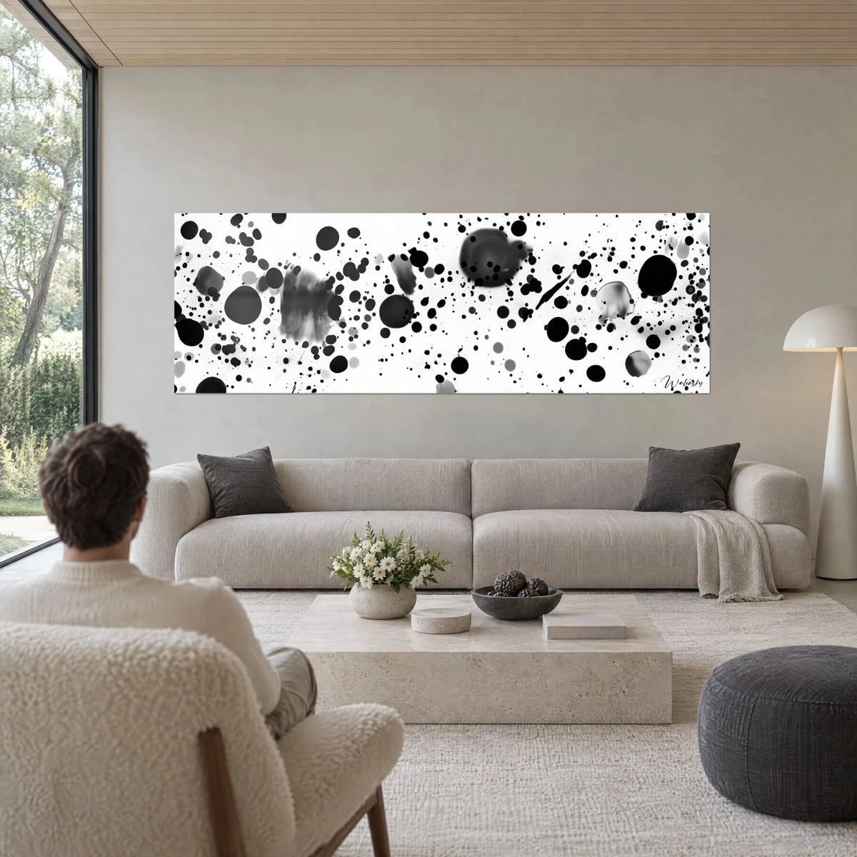 Wall art with black ink splashes on white background, large grey blotches, panoramic format, above a sofa in a bright living room
