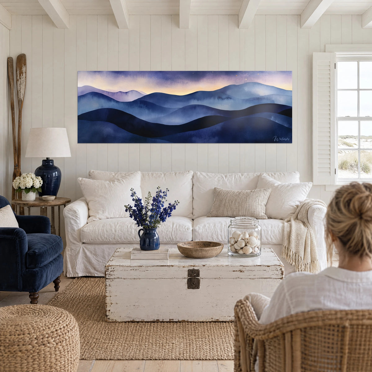 Quadro Colline blu notte ad acquerello, cielo viola con un bagliore dorato, due persone di spalle sopra un divano in un soggiorno luminoso