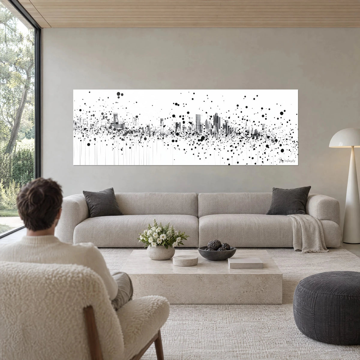 Wall art of a shattered skyline in black ink, grey skyscrapers and droplets on a white background, above a sofa in a bright living room