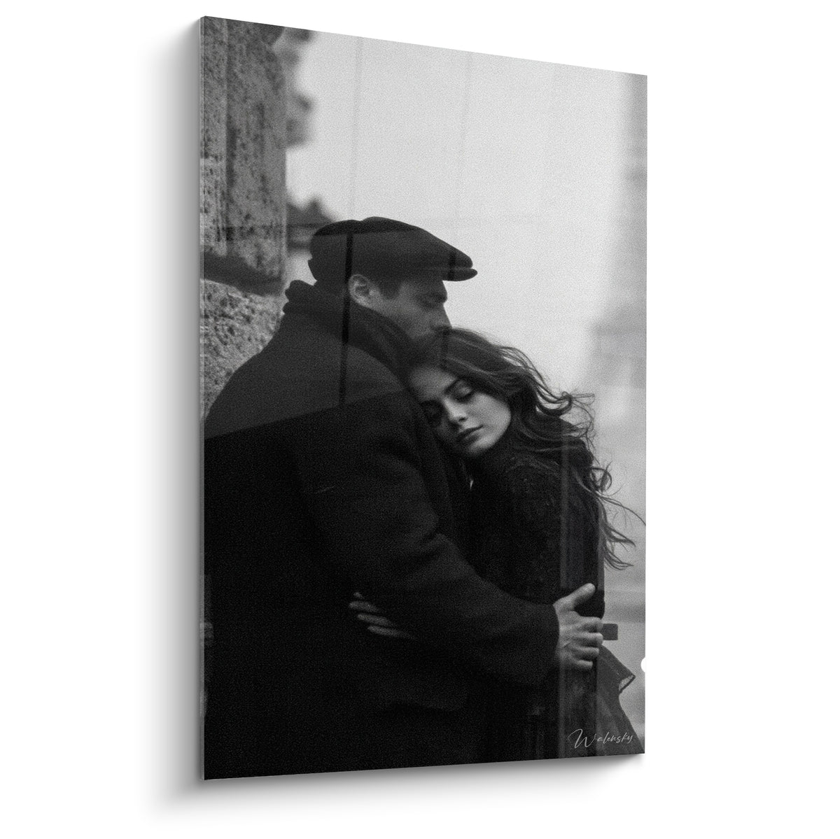 Couple enlacé en noir et blanc, casquette sombre et cheveux bruns, brume architecturale en fond