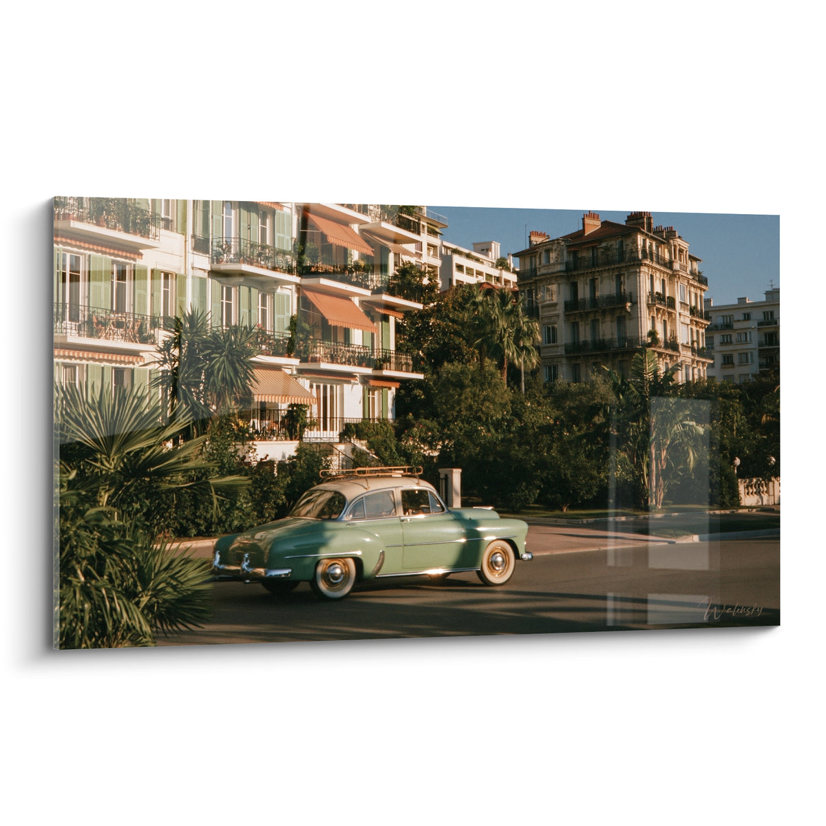 Wall art of an almond green car with an ivory roof driving past ochre facades bathed in golden light