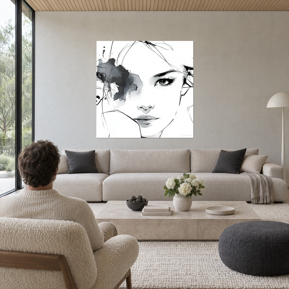 Cuadro retrato de mujer en tinta negra, mirada rodeada por una mancha gris sobre fondo blanco, encima de un sofá en un salón luminoso