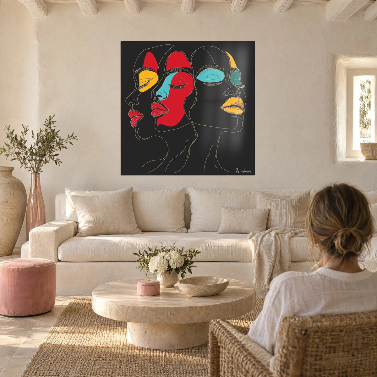Schilderij met drie vrouwengezichten in gouden lijnwerk, rode en gele lippen, turquoise oogleden op zwarte achtergrond, boven een bank in een lichte woonkamer