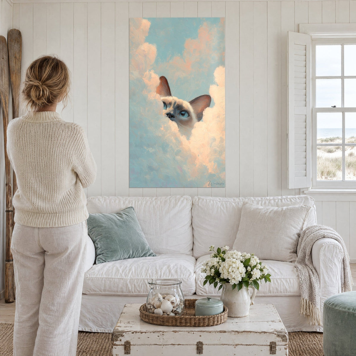 Tableau chat tonkinois aux yeux bleus surgissant d'un nuage rose pêche, ciel turquoise pâle, au-dessus d'un canapé dans un salon lumineux