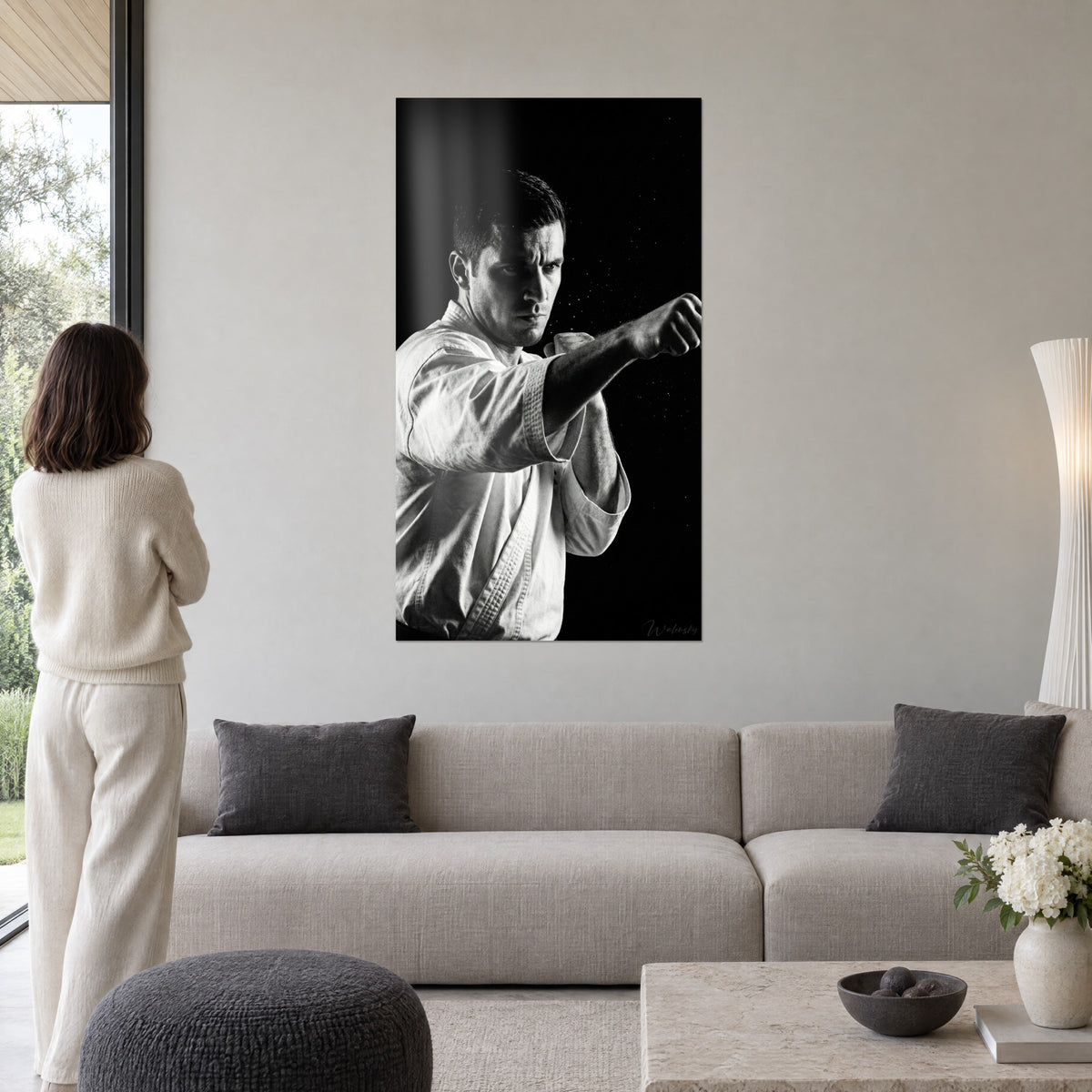 Cuadro de karateka con puño extendido en blanco y negro, kimono blanco brillante sobre fondo negro, encima de un sofá en un salón luminoso
