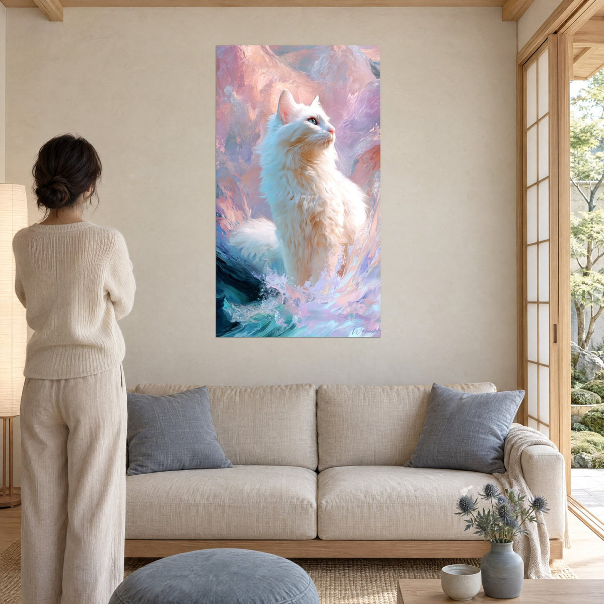 Tableau chat blanc au regard bleu tourné vers le ciel, fond rose et turquoise, femme de dos, au-dessus d'un canapé dans un salon lumineux