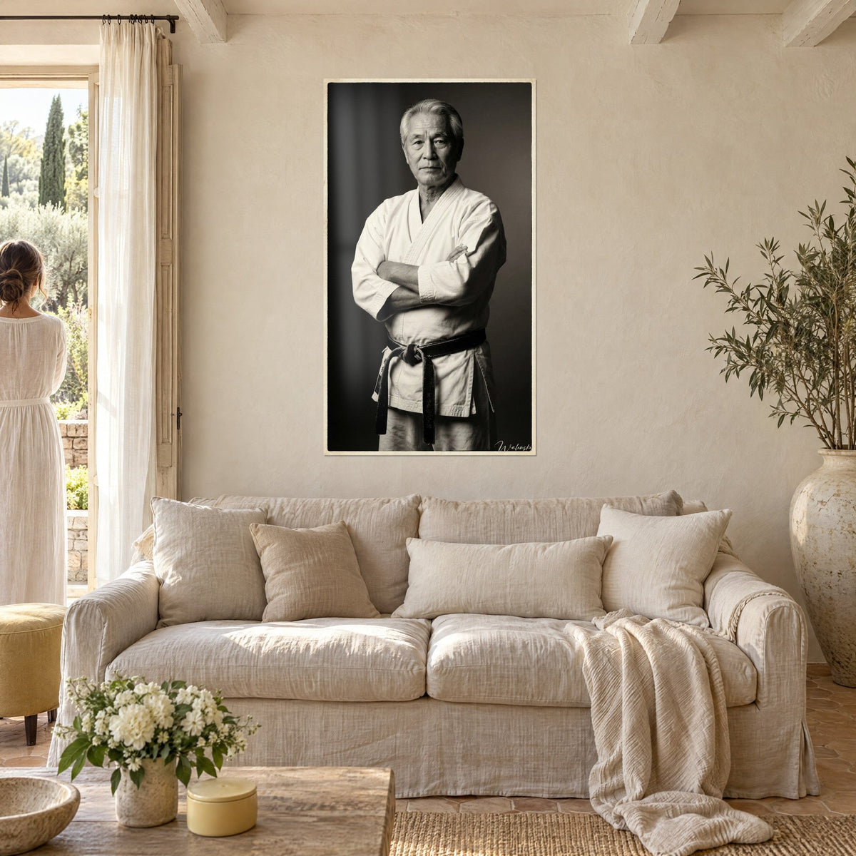 Tableau maître de karaté aux bras croisés, kimono blanc et ceinture noire sur fond gris, au-dessus d'un canapé dans un salon lumineux