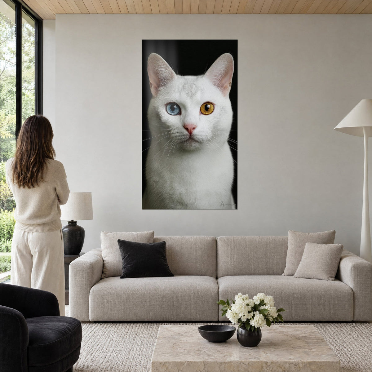 Schilderij witte kat met ongelijke ogen, één blauw, één amber, zwarte achtergrond, vrouw van achteren, boven een bank in een lichte woonkamer