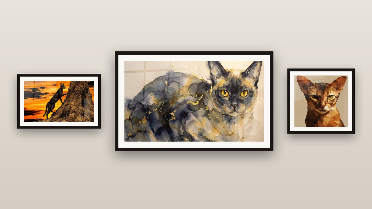 Pared de galería con tres cuadros enmarcados: Gato Chausie Atardecer, Gato Birmano Acuarela y Gato Abisinio Poligonal