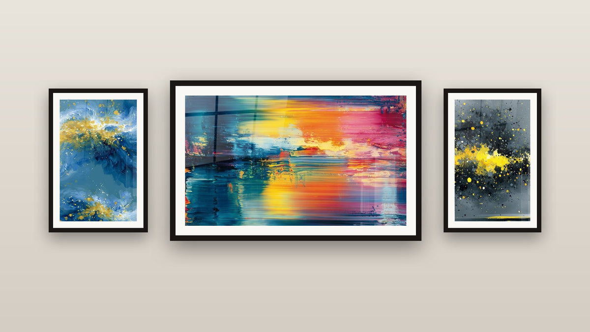 Pared de galería con tres cuadros enmarcados, entre ellos Abstracto colorido y Salpicaduras doradas sobre fondo antracita