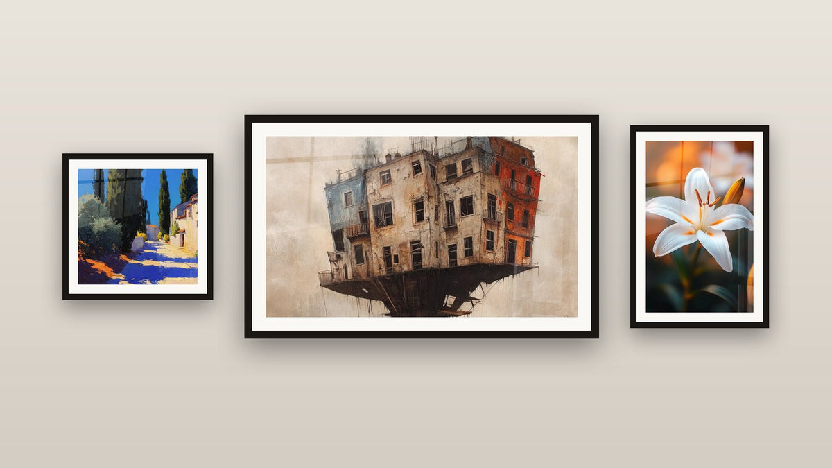 Mur de galerie avec trois tableaux encadrés : Village méditerranéen, Bâtiment Suspendu et Lys N°2