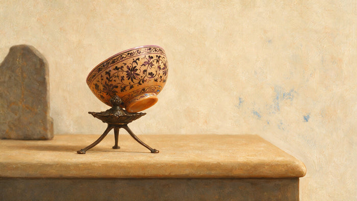 Une petite coupe de porcelaine ocre-orangé sur un trépied, présentée dans une vitrine éclairée avec douceur.