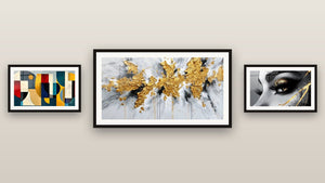 Mur de galerie avec trois tableaux encadrés, dont Explosion dorée sur fond blanc et gris et Formes géométriques colorées