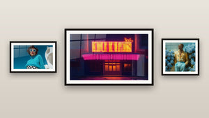 Pared de galería con tres cuadros enmarcados, entre ellos Mujer jersey turquesa gafas redondas y Cine Retro