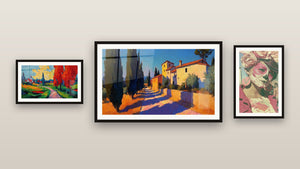 Pared de galería con tres cuadros enmarcados, entre ellos Paisaje campestre colorido y Pueblo mediterráneo