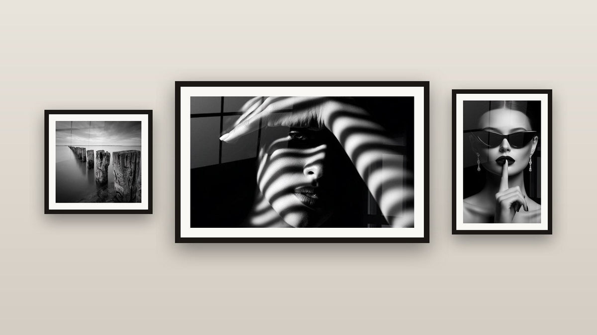 Pared de galería con tres cuadros enmarcados, entre ellos Pilotes de madera en el agua y Mujer Sombras Rayadas