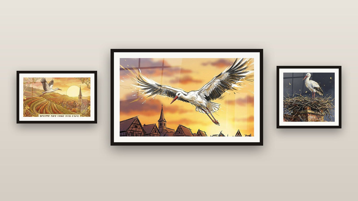 Mur de galerie avec trois tableaux encadrés : Cigogne Alsacienne, Cigogne sur Cheminée et Cigogne Alsace