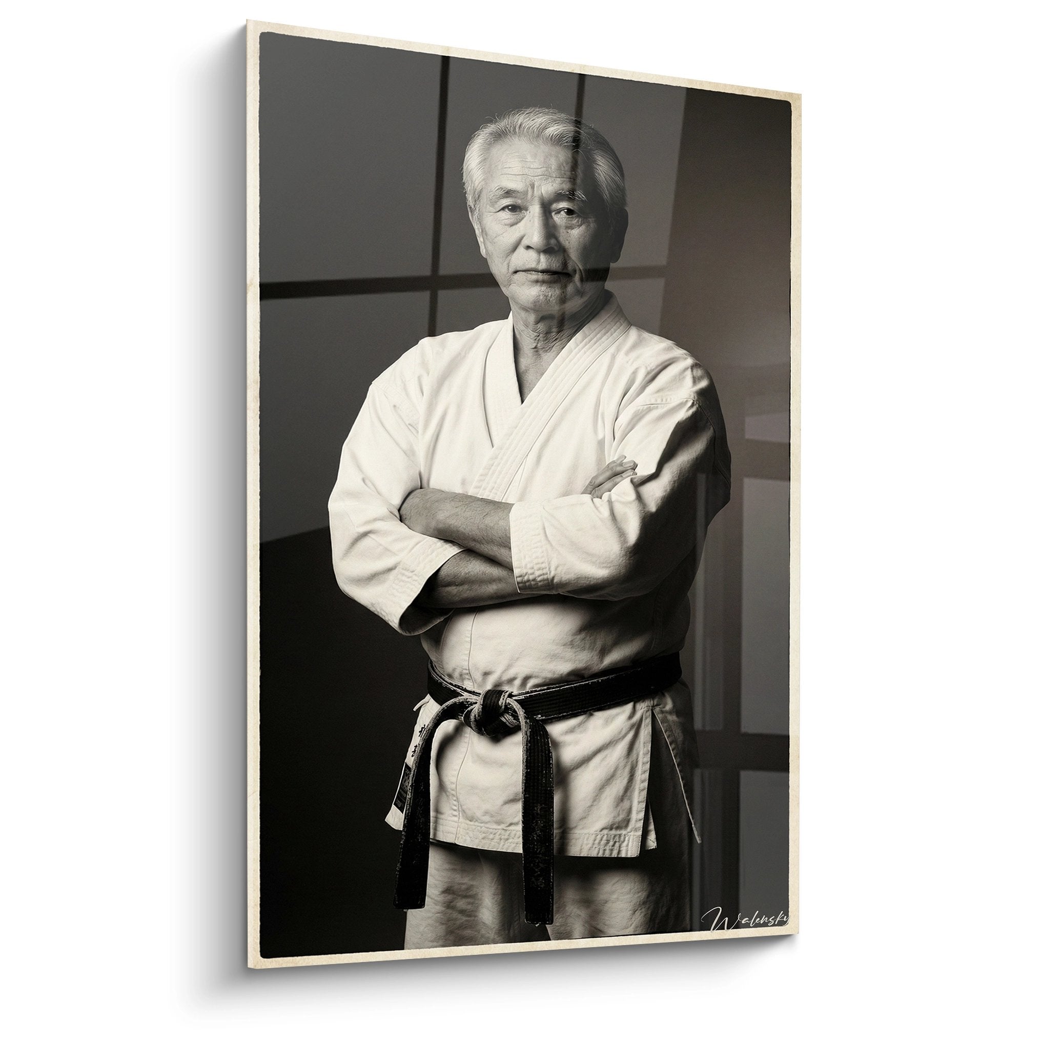 Portrait noir et blanc d'un maitre de karate age en kimono blanc avec ceinture noire, bras croises, dans un dojo