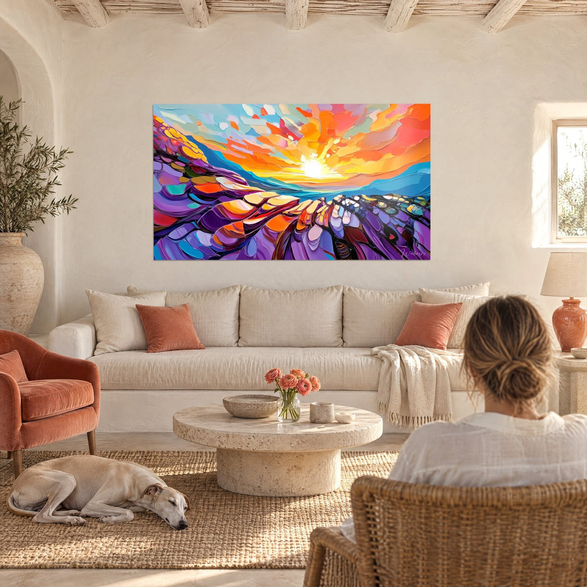 Tableau soleil couchant en pâte épaisse, nuages orange et corail sur crêtes violettes, femme de dos au-dessus d'un canapé dans un salon lumineux