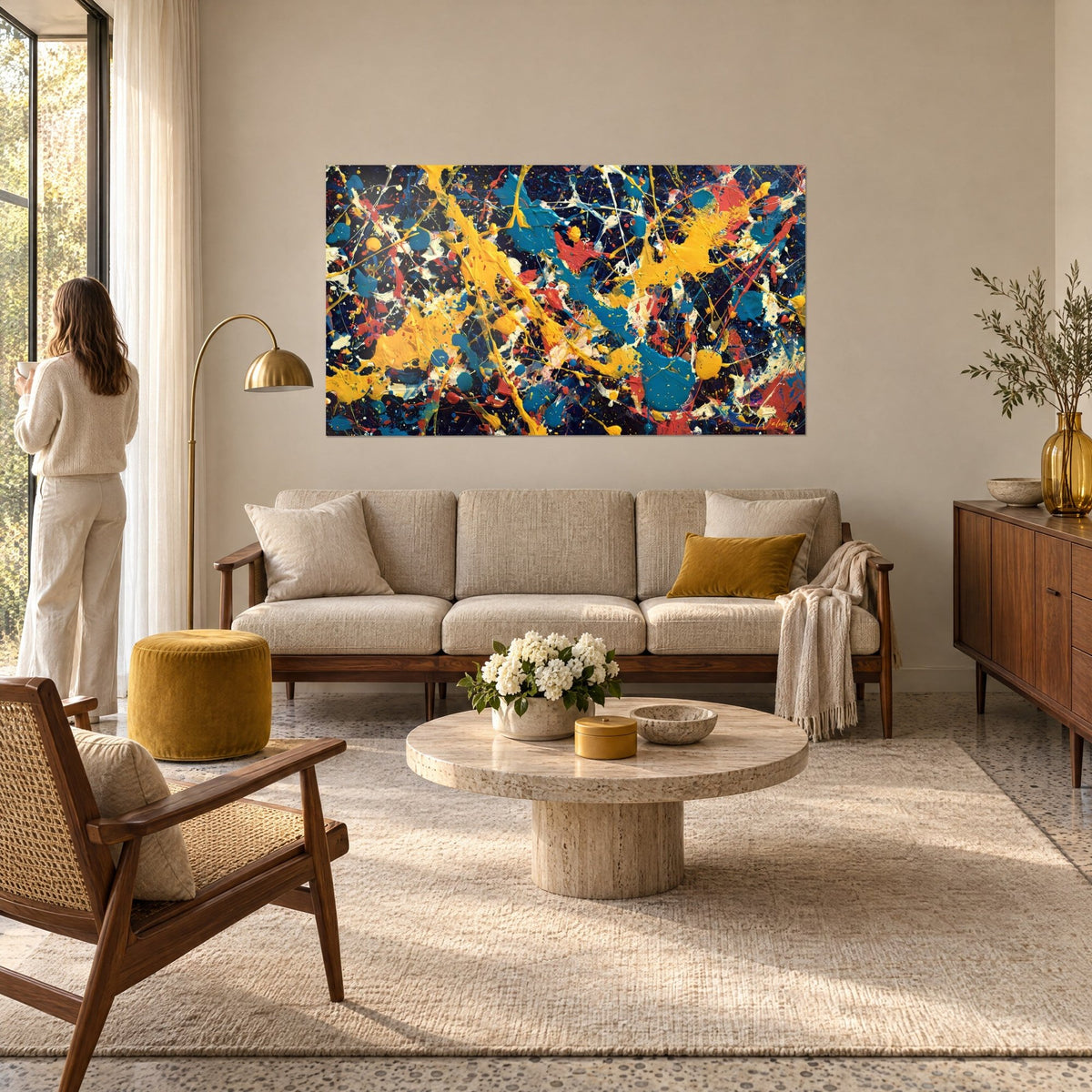 Schilderij met gele en turquoise verfspatten op een nachtblauwe achtergrond, vrouw van achteren, boven een bank in een lichte woonkamer