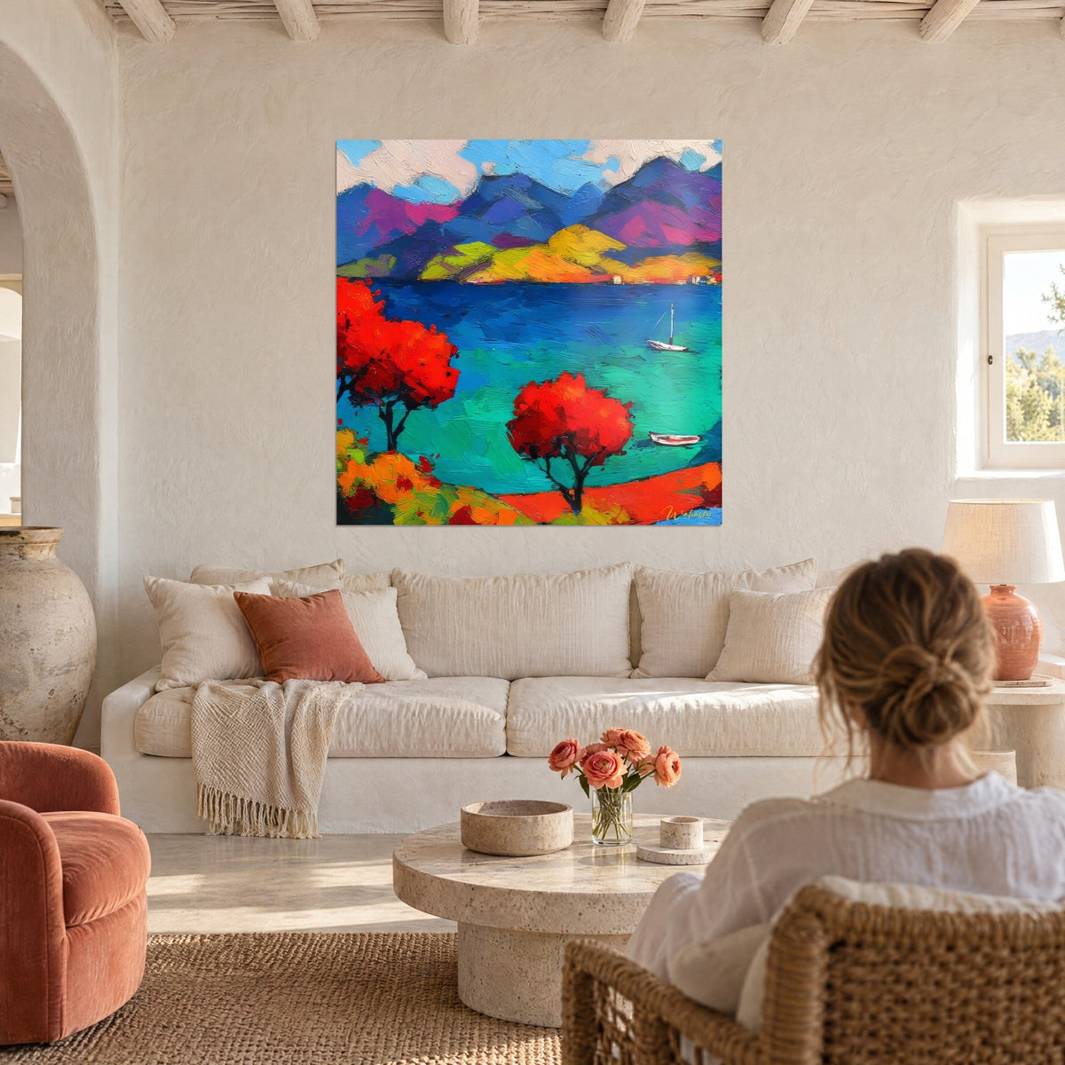 Tableau baie turquoise bordée d'arbres rouges, voilier blanc et collines violettes, au-dessus d'un canapé dans un salon lumineux