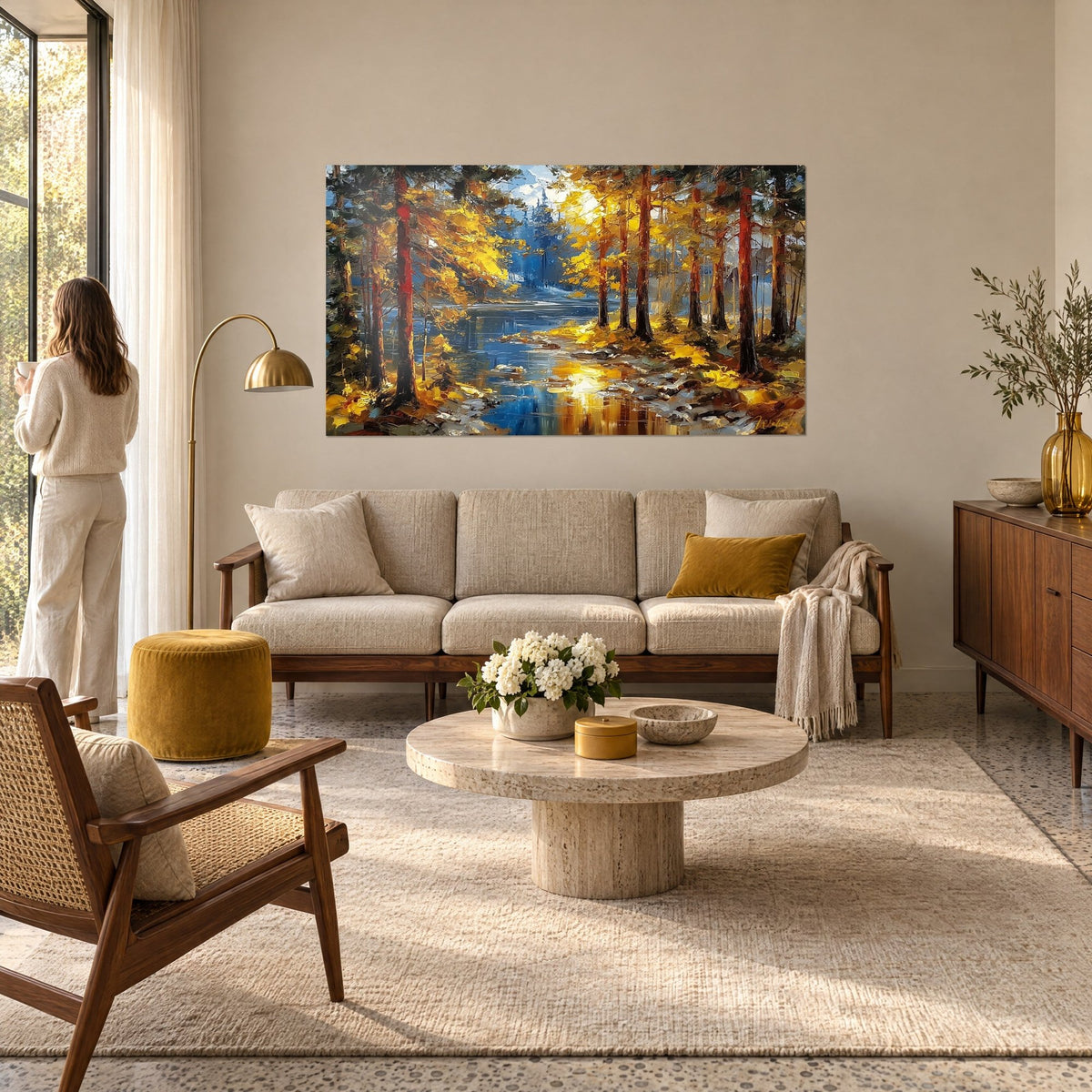 Quadro sottobosco autunnale con fogliame giallo oro e tronchi color ruggine, fiume blu, donna di spalle, sopra un divano in un soggiorno luminoso