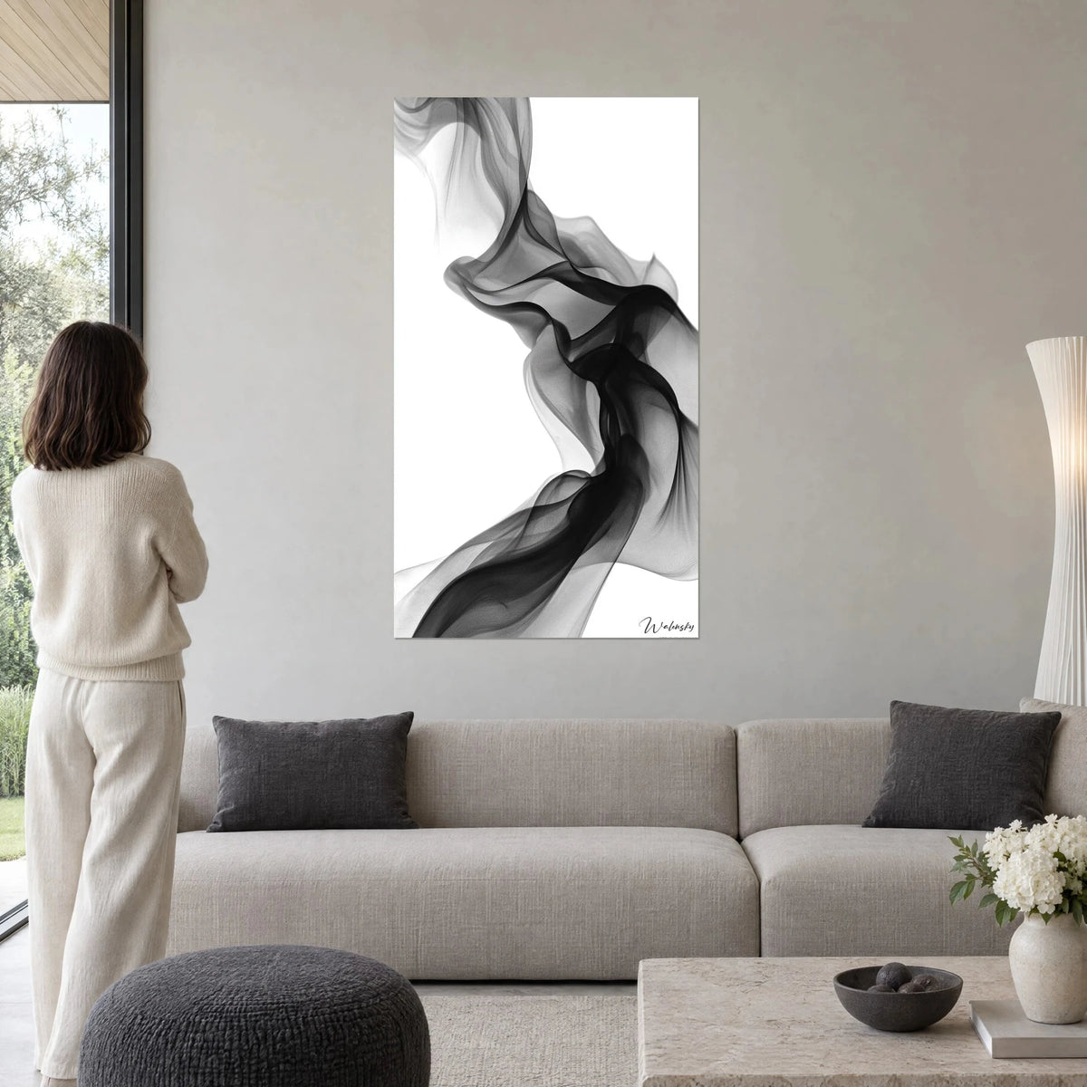 Tableau fumée élégante en volutes noires et grises sur fond blanc pur, femme de dos, au-dessus d'un canapé dans un salon lumineux