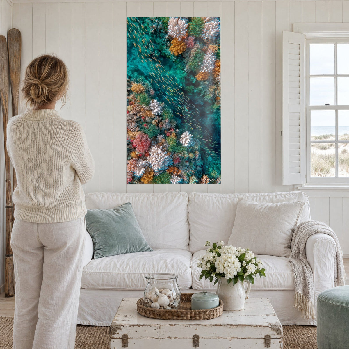Wall art aerial view of a coral reef, turquoise and orange, shoal of golden fish, above a sofa in a bright living room