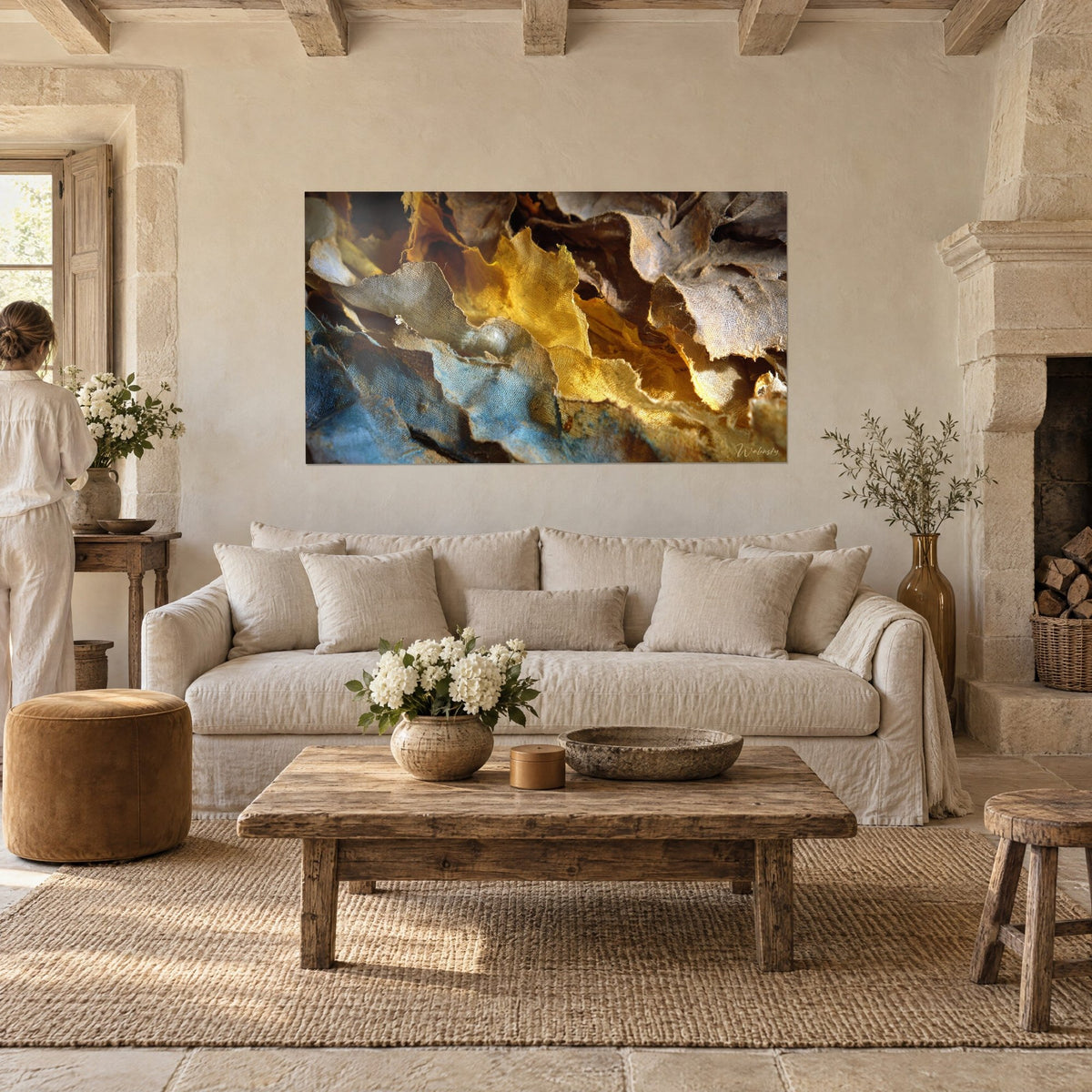 Wall art with tatters of gold gauze and faded blue, frayed mesh, seen from behind by two people, above a sofa in a bright living room