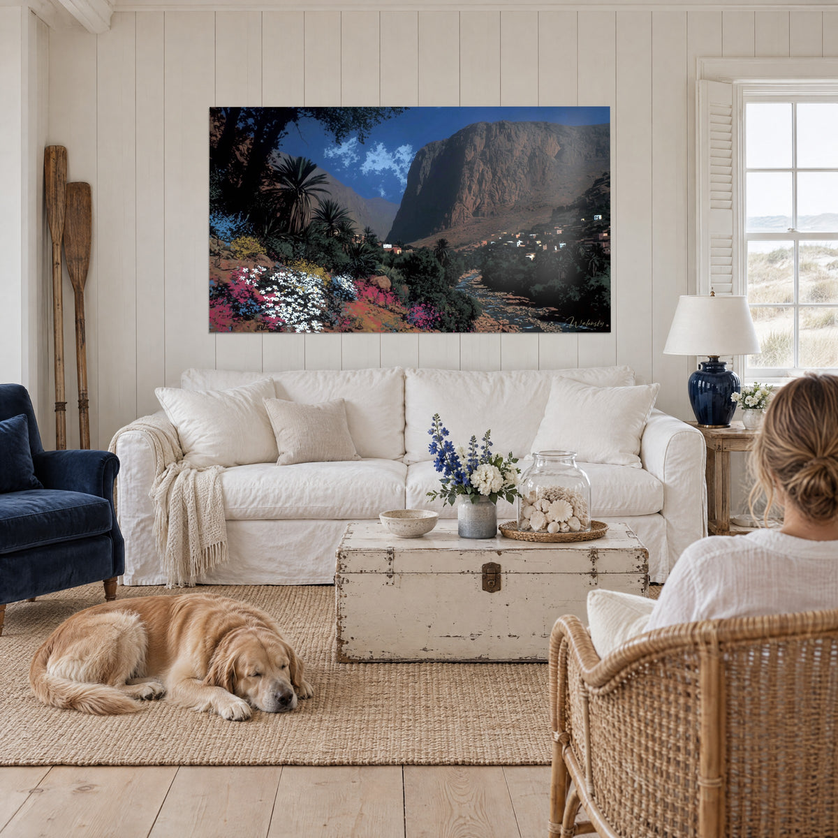 Tableau oasis marocaine sous falaise ocre, fleurs blanches et roses, ciel bleu, au-dessus d'un canapé dans un salon lumineux